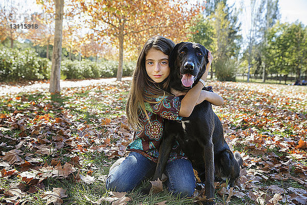 Porträt eines Mädchens mit schwarzem Hund  das im Herbst im Park sitzt