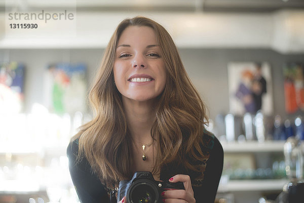 Porträt einer glücklichen Frau  die eine Kamera hält  während sie zu Hause steht