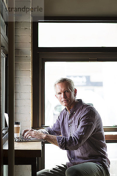 Porträt eines seriösen reifen Mannes mit Laptop am Tisch im Cafe