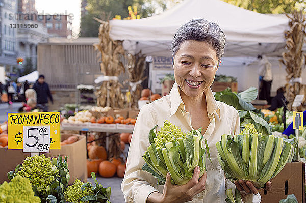 Glückliche reife Frau inspiziert Romanesco-Brokkoli auf dem Bauernmarkt