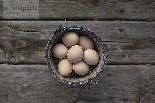 Draufsicht auf braune Eier im Eimer auf Holztisch