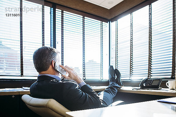 Geschäftsmann spricht am Smartphone  während er sich im Büro entspannt