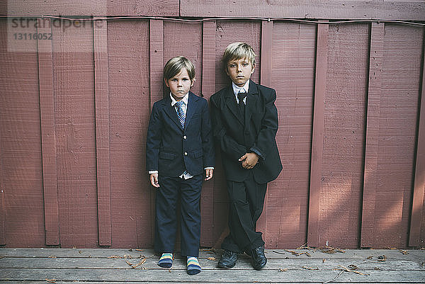 Porträt selbstbewusster Brüder in Anzügen  die an einer Holzwand stehen