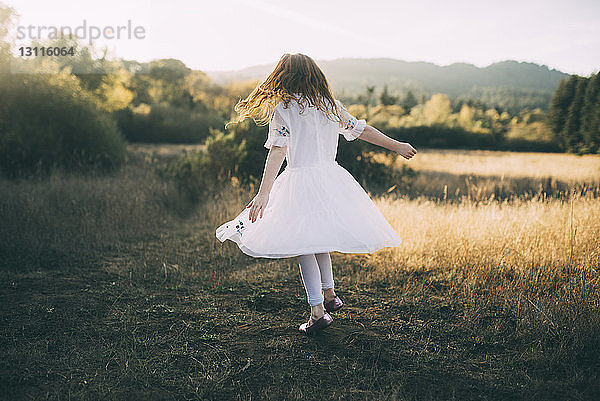 Verspieltes Mädchen in voller Länge in weißem Kleid beim Spinning im Park