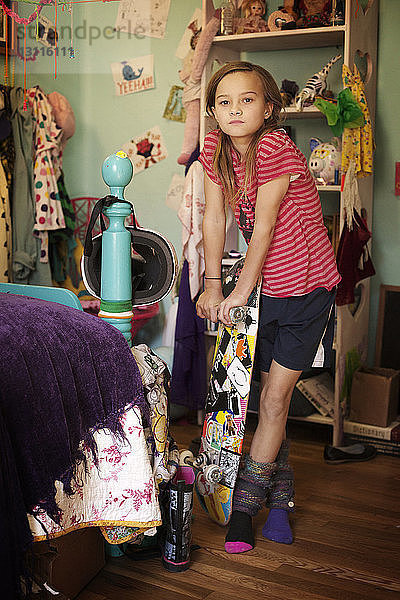 Porträt eines selbstbewussten Mädchens  das im Schlafzimmer stehend ein Skateboard hält