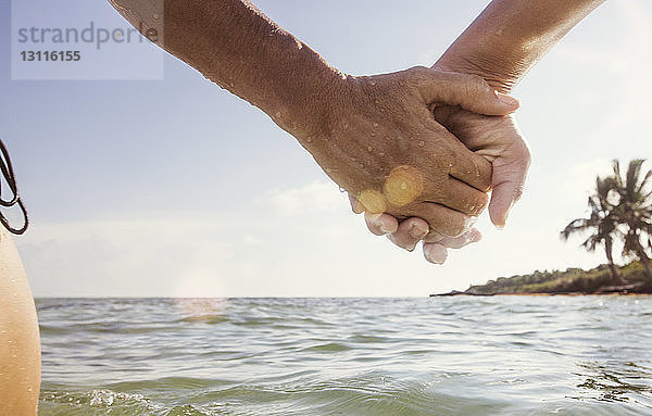 Beschnittenes Bild einer Frau und eines Mädchens  die sich auf dem Meer an der Hand gegen den Himmel halten