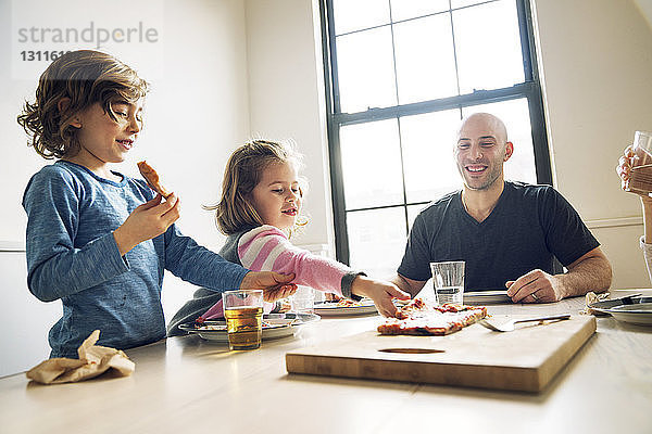 Mädchen pickt Pizzaschnitte  während sie mit der Familie zu Hause am Esstisch sitzt