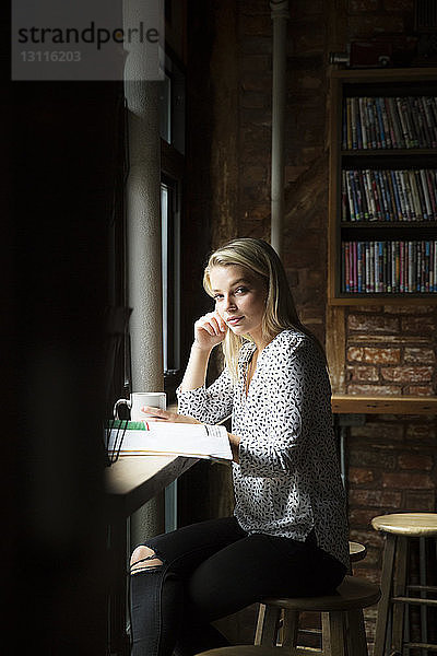 Porträt einer Frau mit Kaffee und Zeitung im Café sitzend