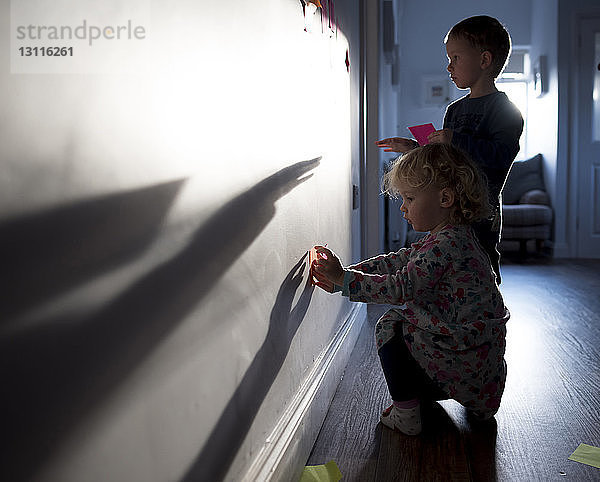 Geschwister kleben zu Hause Haftnotizen an die Wand