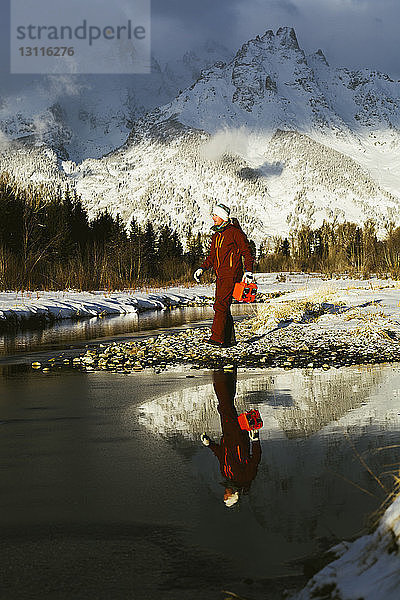 Mann in voller Länge am See vor schneebedeckten Bergen stehend