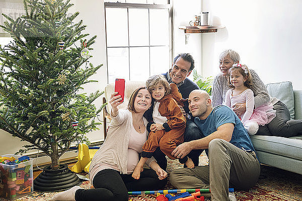 Schwangere Frau  die Selbsthilfe nimmt  während sie mit der Familie zu Hause am Weihnachtsbaum sitzt