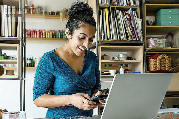 Glückliche Geschäftsfrau benutzt Smartphone  während sie im Büro steht