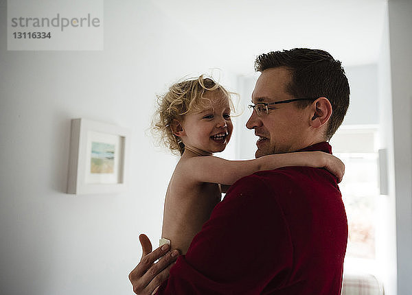 Vater trägt glückliche Tochter  während er zu Hause an der Wand steht