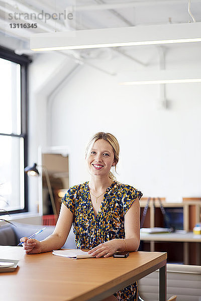 Porträt einer lächelnden Geschäftsfrau  die im Büro am Tisch sitzt