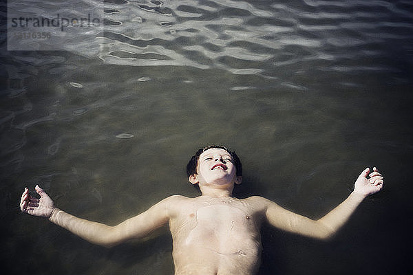 Draufsicht auf einen Jungen ohne Hemd  der bei Sonnenschein auf dem Meer treibt