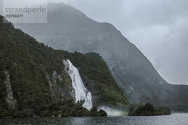 Szenenansicht von Wasserfällen gegen die Berge bei Milford Sound bei nebligem Wetter