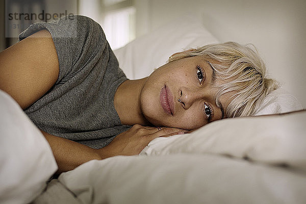 Porträt einer jungen Frau  die zu Hause auf dem Bett liegt