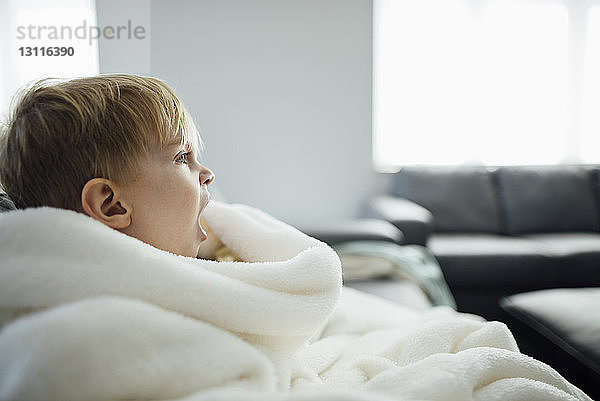 Seitenansicht eines Jungen  der gähnt  während er zu Hause auf dem Sofa sitzt