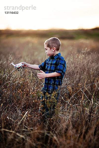 Junge spielt mit Spielzeug  während er auf einem Feld mit Pflanzen gegen den Himmel steht