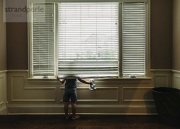 Rückansicht eines Jungen mit Spielzeug  der durch ein Fenster schaut