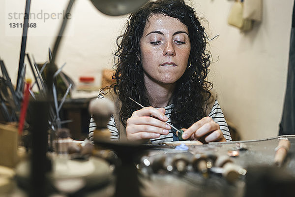 Mitten in einer Werkstatt am Tisch sitzend  in der eine Handwerkerin einen Ring herstellt