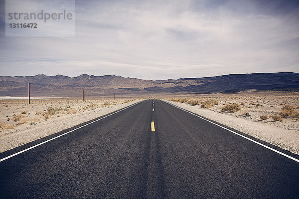 Landstraße  die im Death Valley National Park gegen bewölkten Himmel in Richtung Berge führt