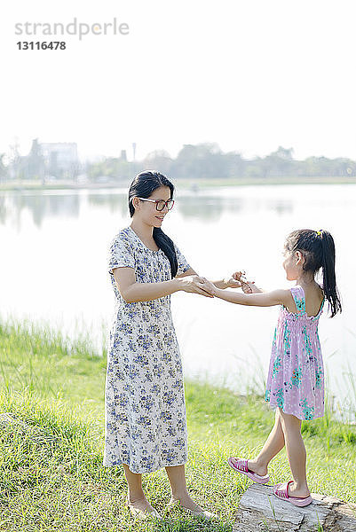 Mutter und Tochter halten sich beim Spielen auf einem Grasfeld am See an den Händen