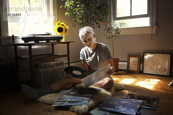 Junge Frau betrachtet Schallplatten  während sie zu Hause auf dem Boden sitzt