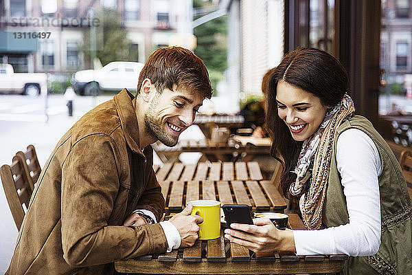 Glückliches Paar schaut auf Handy  während es Getränke im Café genießt