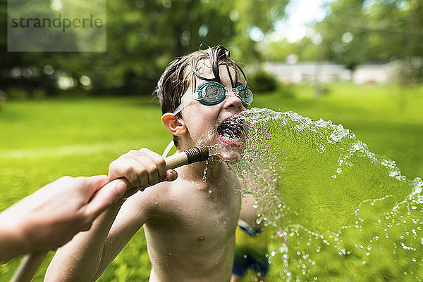 Junge ohne Hemd mit Schwimmbrille beim Spielen mit Wasser im Hof