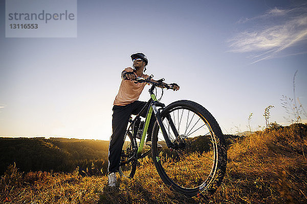 Männlicher Radfahrer schaut weg  während er auf dem Fahrrad gegen den Himmel sitzt