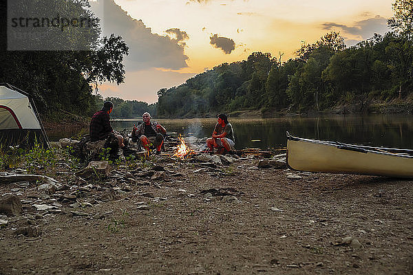 Freunde unterhalten sich beim Camping am See gegen den Himmel bei Sonnenuntergang