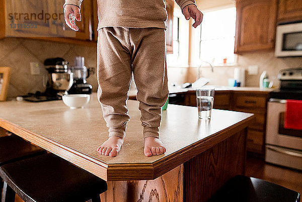 Niedriger Teil eines Jungen  der auf einem Holztisch in der Küche steht
