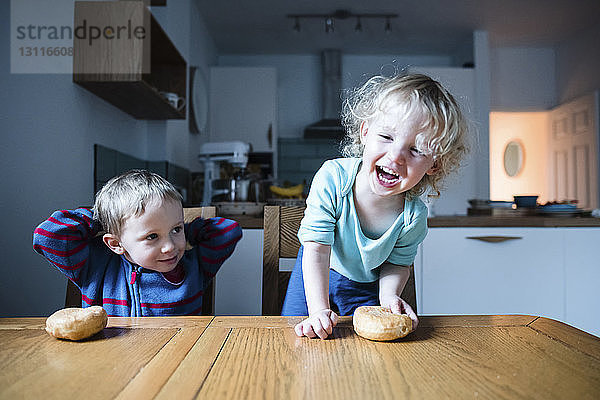 Geschwister mit Brötchen bei Tisch