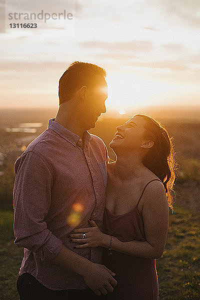Fröhliches junges Paar steht bei Sonnenuntergang auf dem Feld