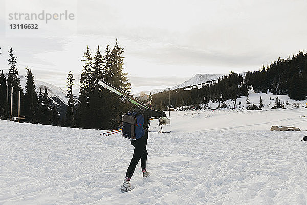 Junge Frau mit Rucksack  die im Winter Skier auf der Schulter trägt