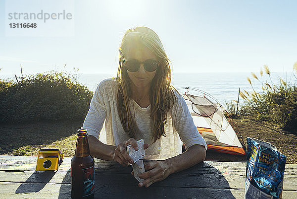 Frau hält Karten  während sie am Tisch auf Feld gegen Meer sitzt