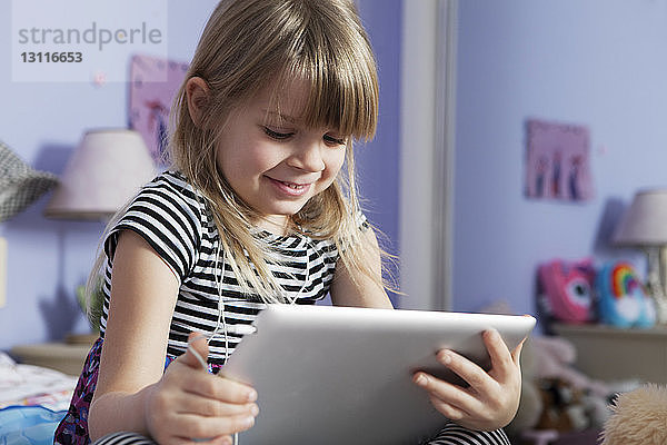 Niedrigwinkelansicht eines glücklichen Mädchens mit digitalem Tablett im Schlafzimmer