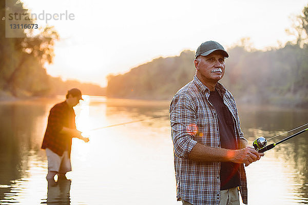 Älterer Mann schaut weg  während ein Freund bei Sonnenuntergang im Hintergrund fischt