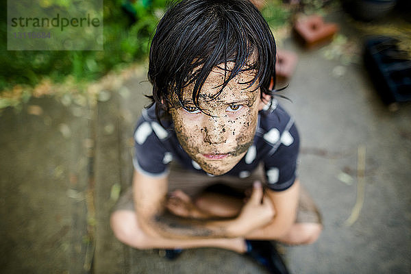 Hochwinkelporträt eines Jungen mit schmutzigem Gesicht  der während der Regenzeit auf einem Fußweg im Hof sitzt