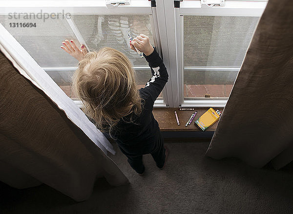 Hochwinkelansicht eines Mädchens  das zu Hause mit Buntstiften am Fenster zeichnet