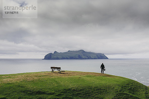 Wanderer schaut auf Aussicht  während er auf einem Hügel am Meer vor stürmischen Wolken steht