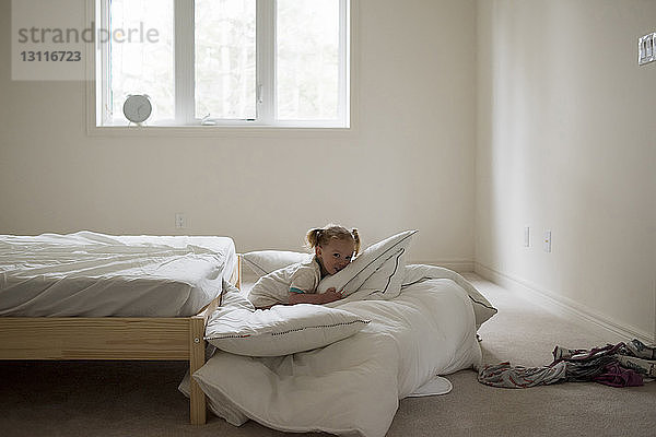 Porträt eines Mädchens  das auf einer Bettdecke neben dem Bett im Schlafzimmer sitzt