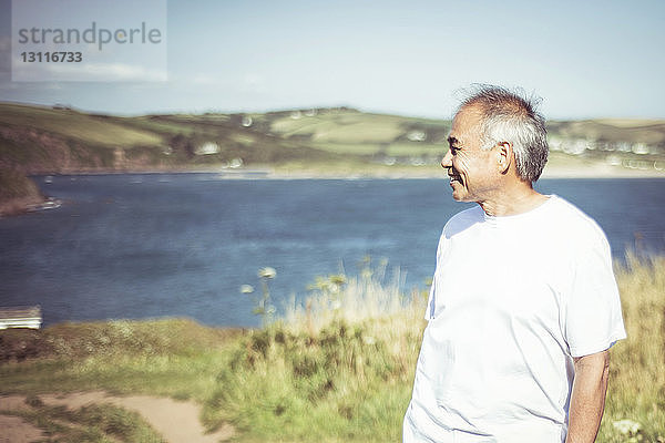 Älterer Mann schaut weg  während er auf dem Feld am See steht