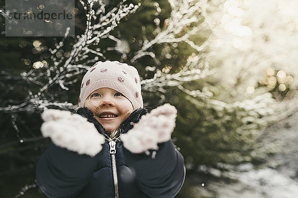 Lächelndes Mädchen spielt im Winter mit Schnee