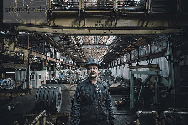 Porträt eines selbstbewussten männlichen Arbeiters  der in einer Fabrik gegen Stahlbleche steht
