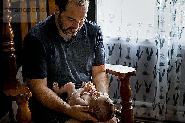 Vater trägt Sohn  während er zu Hause auf Stuhl sitzt