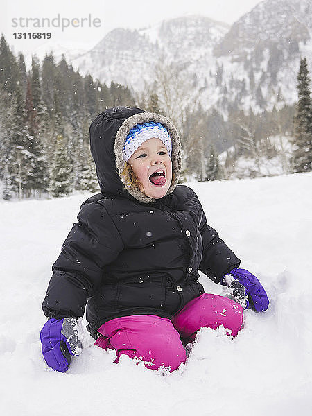 Glückliches kleines Mädchen kniet auf schneebedecktem Feld gegen Berg