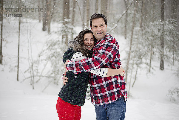 Porträt eines glücklichen Vaters  der seine Tochter umarmt  während er auf einem schneebedeckten Feld im Wald steht
