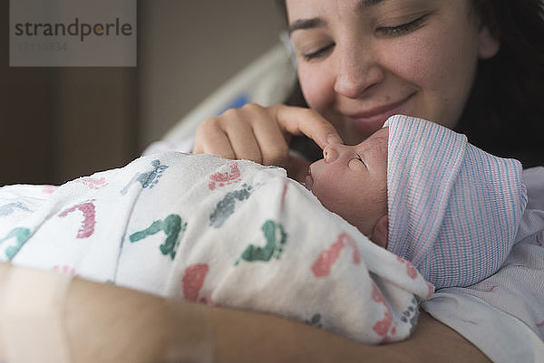 Nahaufnahme einer Mutter  die mit ihrem neugeborenen Sohn spielt  während sie sich im Krankenhaus im Bett ausruht